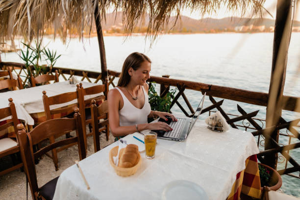 istock Smiling woman using a laptop in a seaside restaurant in Greece 1433175039