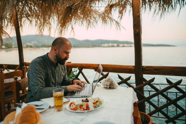 istock Man using a laptop in a seaside restaurant during a vacation 1433175040