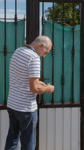 Old man using keys to open a fence door, vertical view stock photo