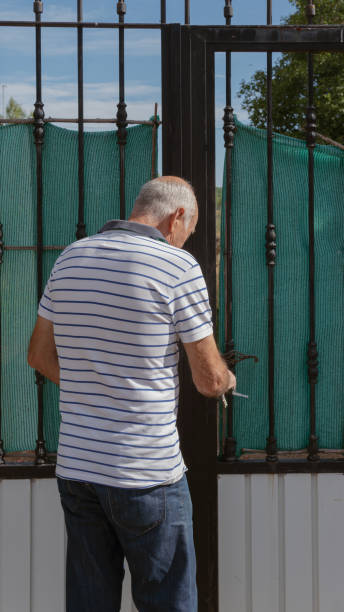 Old man using keys to close a fence door, vertical view stock photo