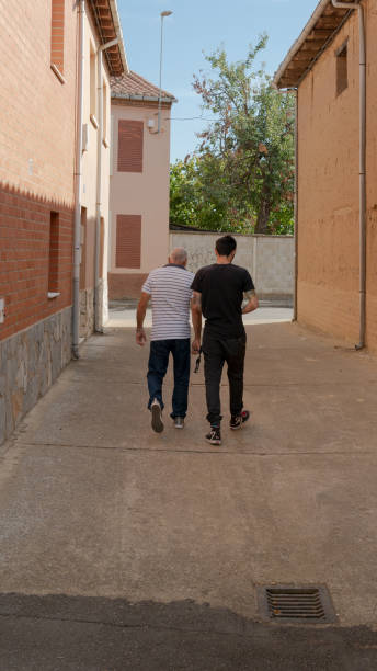 young man and old man walking through an alley - men latin american and hispanic ethnicity southern european descent mature adult imagens e fotografias de stock