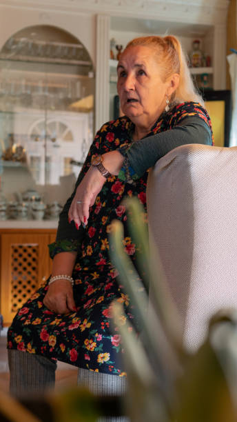 Old woman sitted on the side of an armchair with the mouth open, stunned stock photo