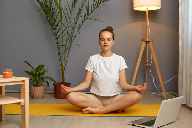 Calm Caucasian woman meditating, practicing yoga online at home, sitting on lotus pose on mat with laptop, breathing fresh air, stress relief, mindful young female involved in internet lesson, webinar mujer caucásica tranquila meditando, practicando yoga en línea en casa, sentada en pose de loto en una colchoneta con computadora portátil, respirando aire fresco, alivio del estrés, joven consciente involucrada en una lección de internet, seminario w