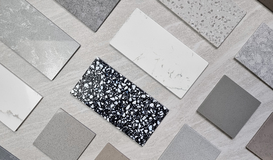 top view interior mood board. material samples palette contains various type, texture and color of artificial stones, marbles, grainy stone tiles, quartzs placed on grey travertine background.