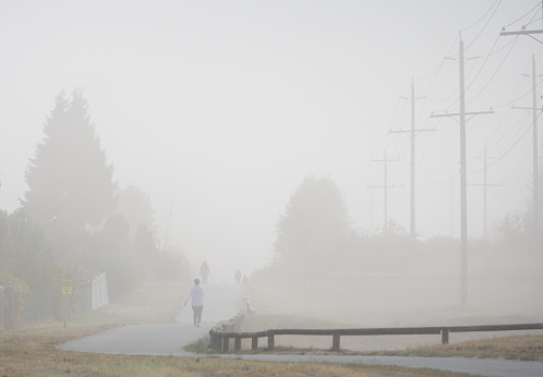 Surrey, Canada - September 29, 2022: Pedestrians walk along the Green Timbers Greenway in the Fleetwood neighborhood of Surrey, British Columbia. Rows of utility poles line the green belt in this residential district. Forest fires and fine particulates in the air contribute to the haze.