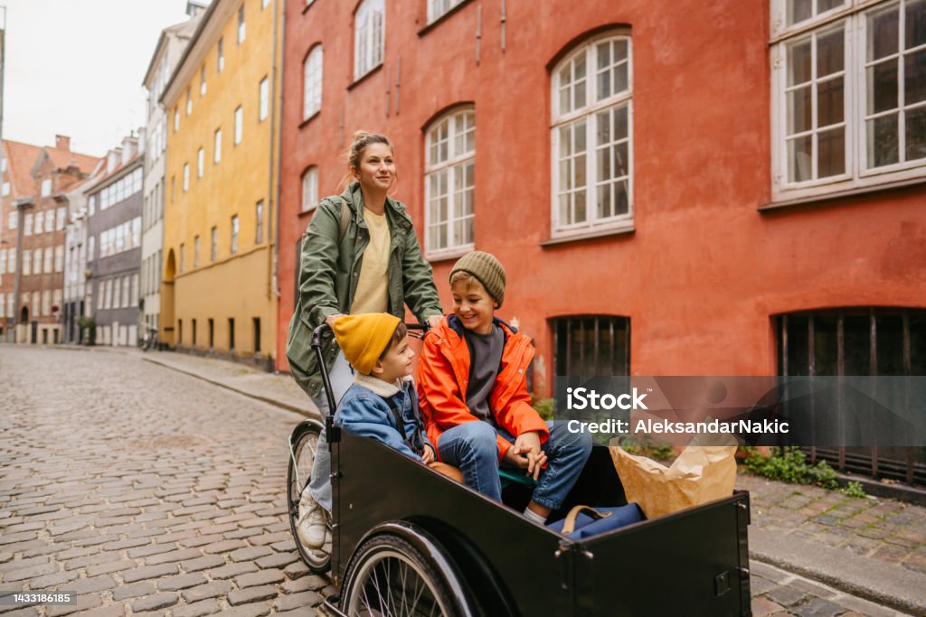 Going back home from school Photo of two boys riding in a cargo bike around the city with their mother; going grocery shopping after school and running errands. Cargo Bike Stock Photo