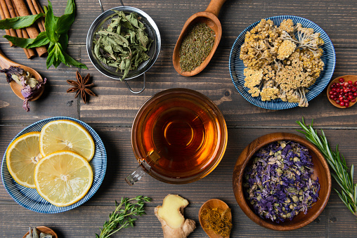 Directly above view of a tea cup with herbal tea  surrounded by a variety of herbal teas and tea ingredients like Chamomile tea, Sage tea, Linden tea, Fennel tea, Melissa tea, Rose tea,  Rosemary Tea , Corn silk tea , anise, cinnamon, thyme, mint, ginger , dried orange slices and rosemary on wooden background.