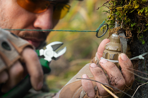 Close-up photo - a sapper clears a booby trap. The wire cutters cutting the wire of the frag grenade trap. Guerrilla war.