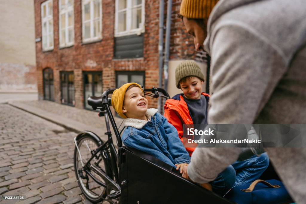 Fasten your seat belts! Photo of a father having fun with his sons and helping one of them fasten his seat belt before their cargo bike ride. Cargo Bike Stock Photo