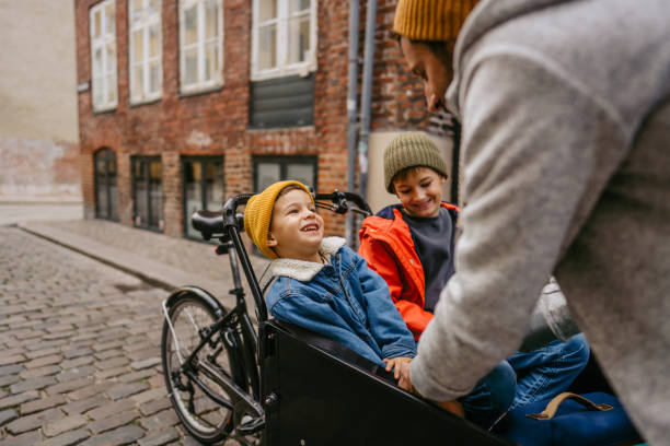 Fasten your seat belts! Photo of a father having fun with his sons and helping one of them fasten his seat belt before their cargo bike ride. bicycle cycling school child stock pictures, royalty-free photos & images