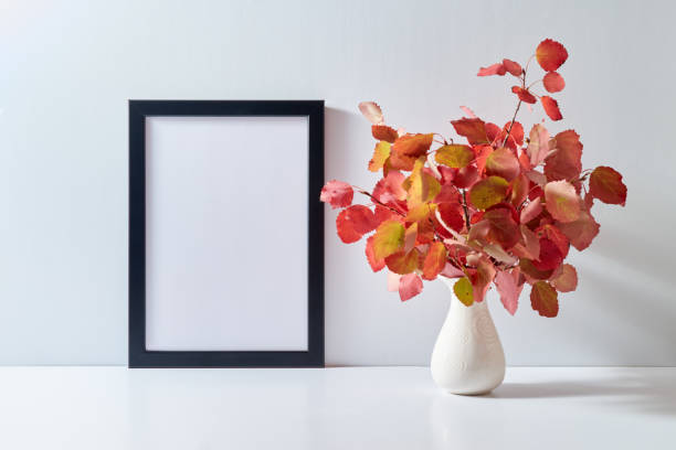 istock Mockup with a black frame and colorful autumn leaves in a vase on a light background. Empty poster frame mockup for presentation design, text, lettering 1433190446