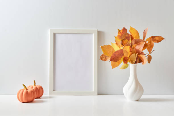 istock Mockup with a white frame and colorful autumn leaves in a vase on a light background. Empty poster frame mockup for presentation design, text, lettering 1433190486