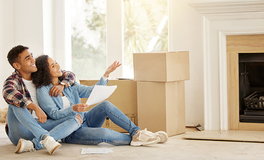 Real estate, house and couple in new home after their property investment as they sit together by boxes on the floor. Interior, smile and young man and woman love investing in residential housing