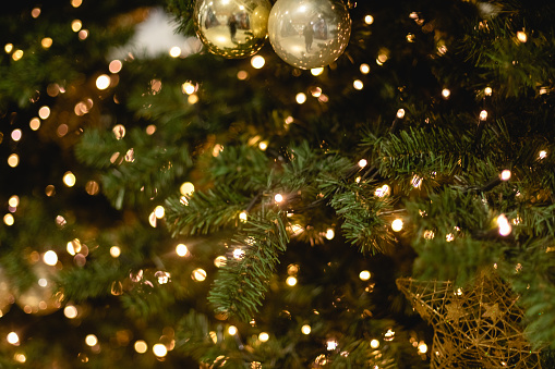 A golden ball, hanging from a Christmas tree, with the surrounding Christmas lights reflecting within