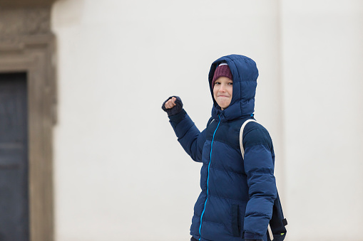 The boy standing in front of a blue jacket with a hood and a backpack in his back