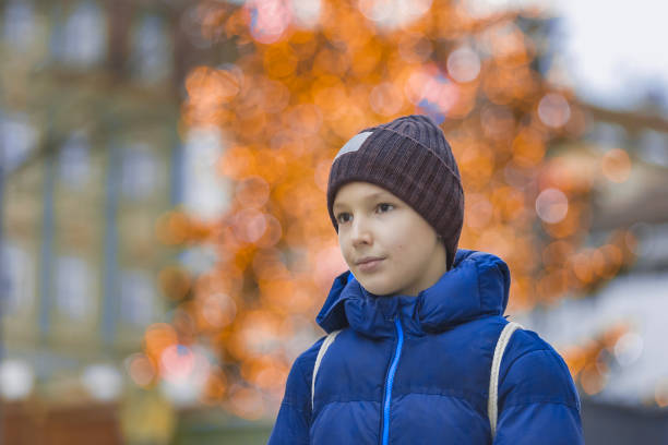 un homme souriant de 12 ans vêtu d’une veste bleue et d’une casquette avec un sac à dos debout dans la rue et derrière lui est un super bokeh - 10 11 years little boys child happiness photos et images de collection
