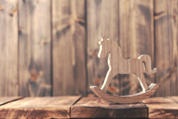 A close-up shot of a wooden rocking horse toy. It is made of light wood with a brown saddle and a tail made of a rope. The rocking horse is on a white background and is in focus. 3D rendering.
