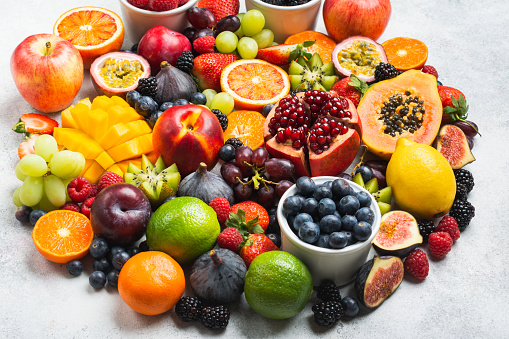 Circle made of healthy raw rainbow fruits, mango papaya strawberries oranges passion fruits berries on oval serving plate on light concrete background, selective focus