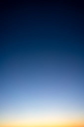 Photograph of a clear evening sky, just after sunset, with a smooth gradient from black down to golden yellow/orange.