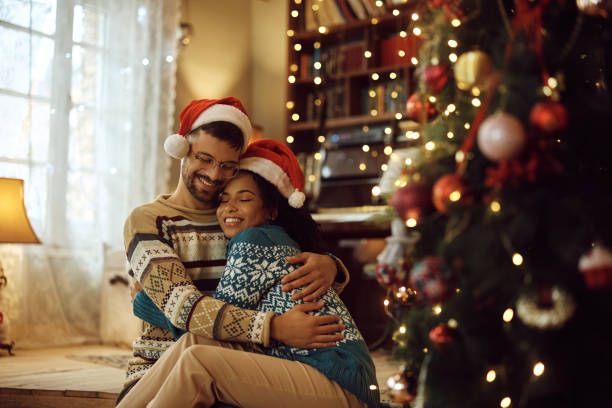 istock Embraced couple with eyes closed sitting by Christmas tree at home. 1433199577