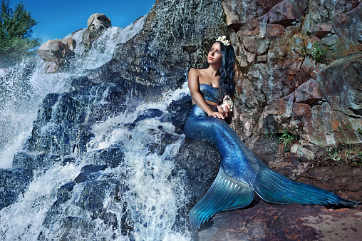 Beautiful mermaid sitting at the waterfall looking to the side