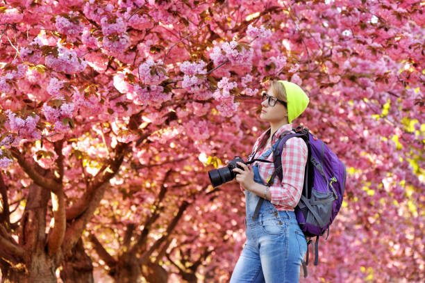 Young woman with a photo camera walking under blooming trees