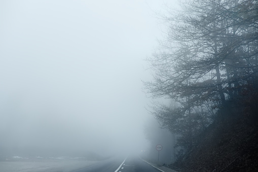 Thick fog on the highway in Europe on a winter day. The danger of driving of vehicles on roads in bad foggy and rainy weather. Insurance of safety of drivers and cars.