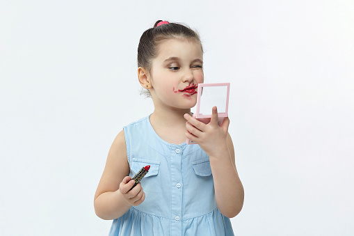 little black-haired girl paints her lips with red lipstick. funny photo shoot in the studio on a white background.