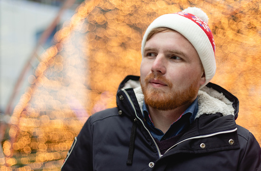 Male portrait of adult bearded man, wear red Christmas Santa Claus hat outdoors. New year concept photo at the street