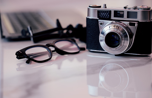 Closeup of a camera and glasses on a desk in an office. Blogger or photographer's workstation at home of in a modern office