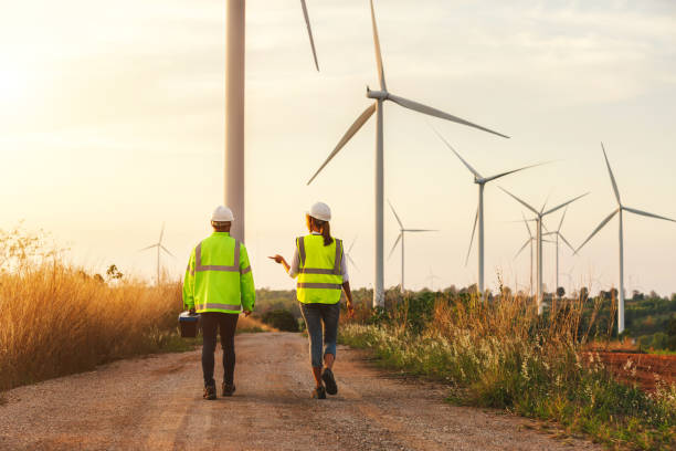 Back view of young maintenance engineers team working in wind turbine farm at sunset. Back view of young maintenance engineers team working in wind turbine farm at sunset. mill stock pictures, royalty-free photos & images