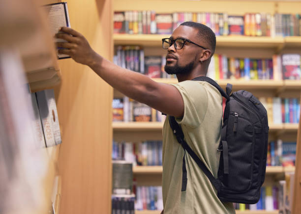 istock College or university student in a library taking a book from the shelf to read and study for education. Reading, learning and academic black man nerd at a bookstore to buy a textbook 1433217373