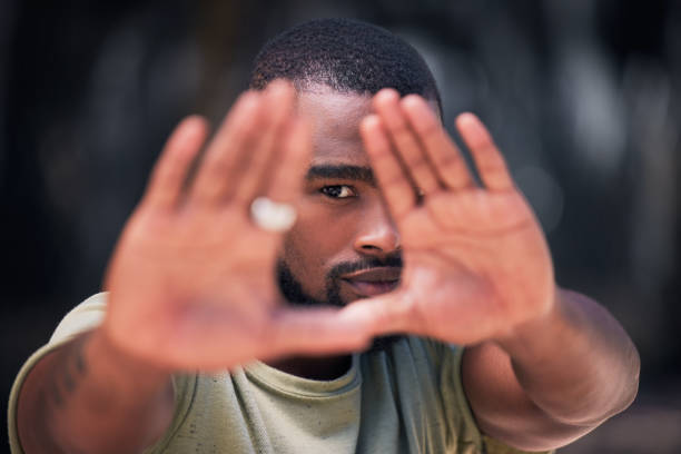 istock One handsome young trendy african american man using his two hands to frame his face for a photograph in a city. Serious black man expressing with his hands up in protest against human rights downtown 1433221346