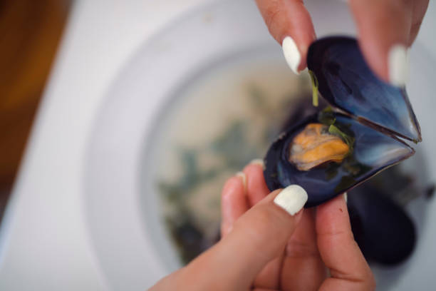 An unrecognizable woman eats mussels. Mussels are edible sea shells.