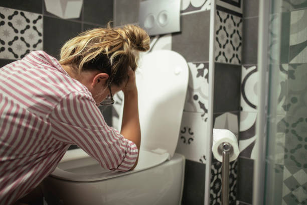 Desperate woman vomits leaning on an open toilet seat in her bathroom stock photo