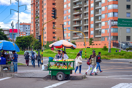 Bogota, Colombia - May 19, 2017: This is the road intersection where Calle 134 cuts across Carrera Novena in the Latin American Andes capital city of Bogotá. A local street-side fruit seller is seen selling fruits to passers-by. In the background is a residential building. Traffic moves up and down Calle 134. The altitude at street level is 8,660 feet above mean sea level.  Horizontal Format.