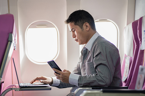young man working on plane and holding smartphone and laptop
while sitting in the cabin of an airplane work and travel concept