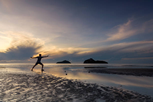 istock A man silhouette practicing yoga on the beautiful beach at sunrise, 1433252365
