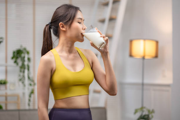 atractiva mujer asiática de fitness terminando el entrenamiento y bebiendo vitaminas de batido de leche de proteína después de entrenar en casa. culturismo. estilo de vida saludable. - mujer bebiendo leche fotografías e imágenes de stock