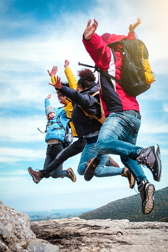 Group of young happy friends having fun and jumping in top of the mountain - Hikers with backpacks celebrating success outdoor - People, success and sport concept