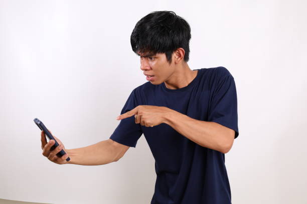 istock Angry young asian man standing while talking on the phone. Isolated on white background 1433266903