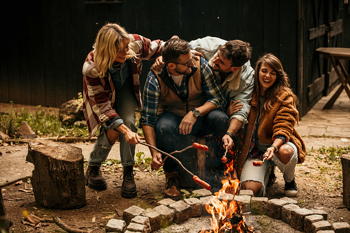 A Group of mature female and male friends in their 30s and 40s gathered around a fire pit in a cabin forest house.