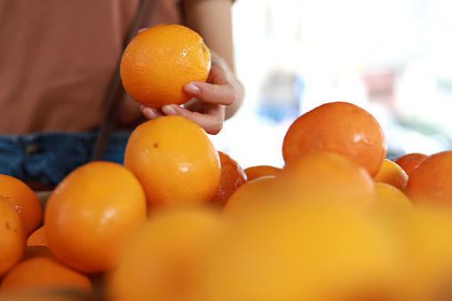 Woman's hand choosing fresh orange fruit in supermarket. Concept of healthy vegetarian food.