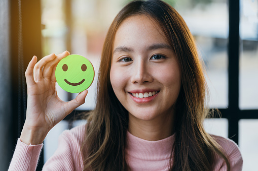 Hands of woman holding happy smile face on wood block, user giving good feedback rating, think positive , customer review, assessment, of mental health day, Compliment Day, satisfaction concept.
