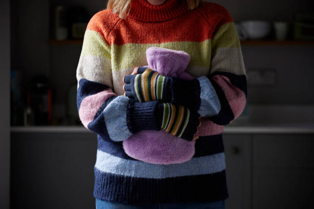 mulher de luvas abraçando garrafa de água quente tentando se manter aquecida durante crise de energia do custo de vida - hot water bottle - fotografias e filmes do acervo