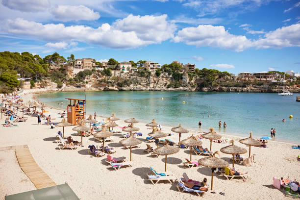 Porto Cristo beach resort, eastern coast of Mallorca Vacationers relaxing under umbrellas and enjoying calm, crystal clear water of natural inlet. Homes on cliffs in background. walking in water stock pictures, royalty-free photos & images