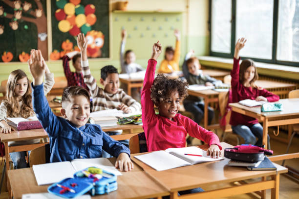 studenti elementari felici alzano le mani su una classe a scuola. - child classroom education school foto e immagini stock