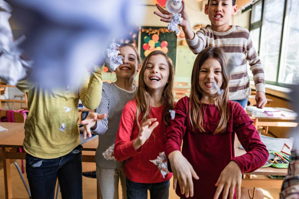 istock Happy school children throwing crumpled papers in the classroom. 1433287870