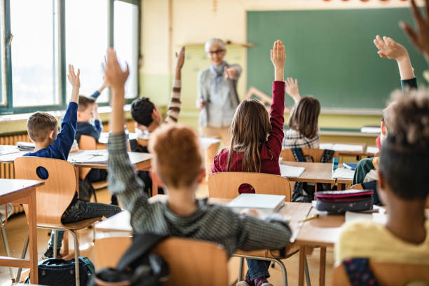 istock Back view of students raising their hands to answer the teacher's question on a class. 1433288527