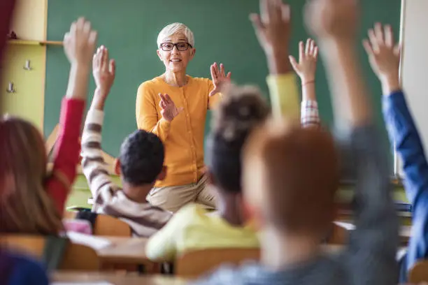 Senior teacher aiming at her elementary students while wanting to hear the answers to her question.